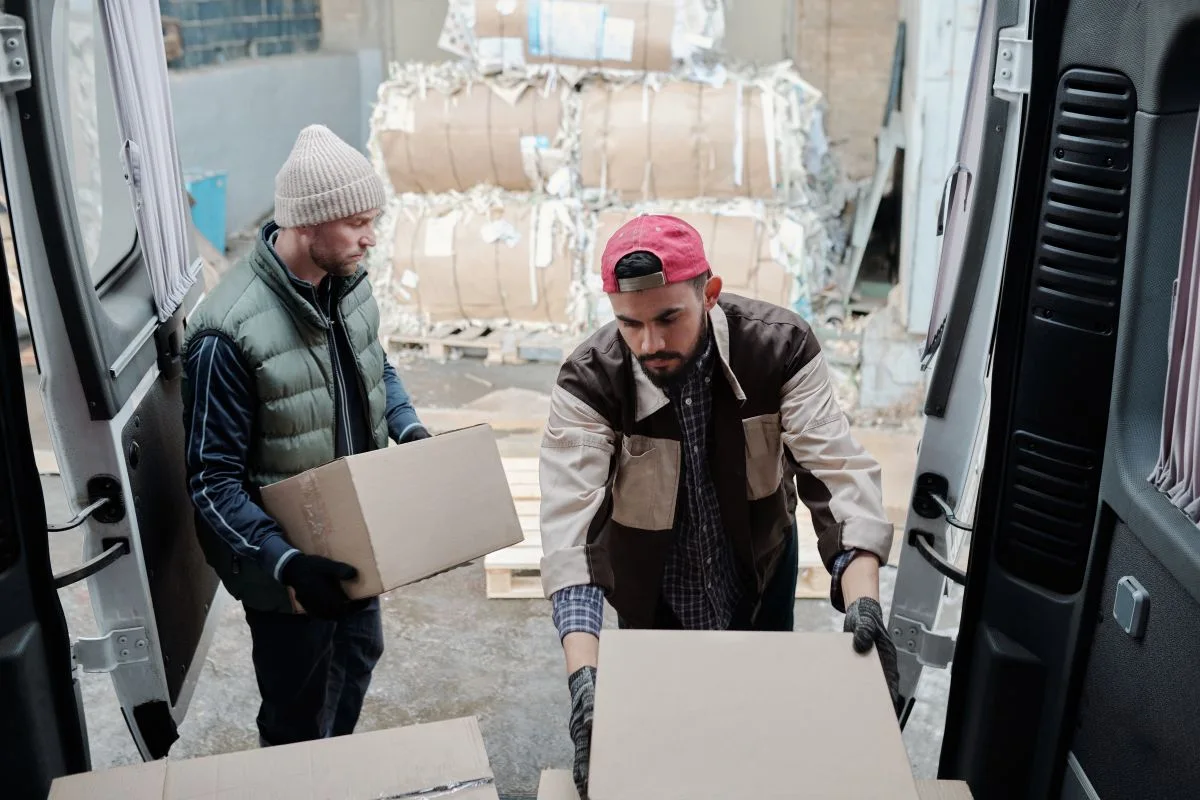 Two workers carrying boxes beside an open van